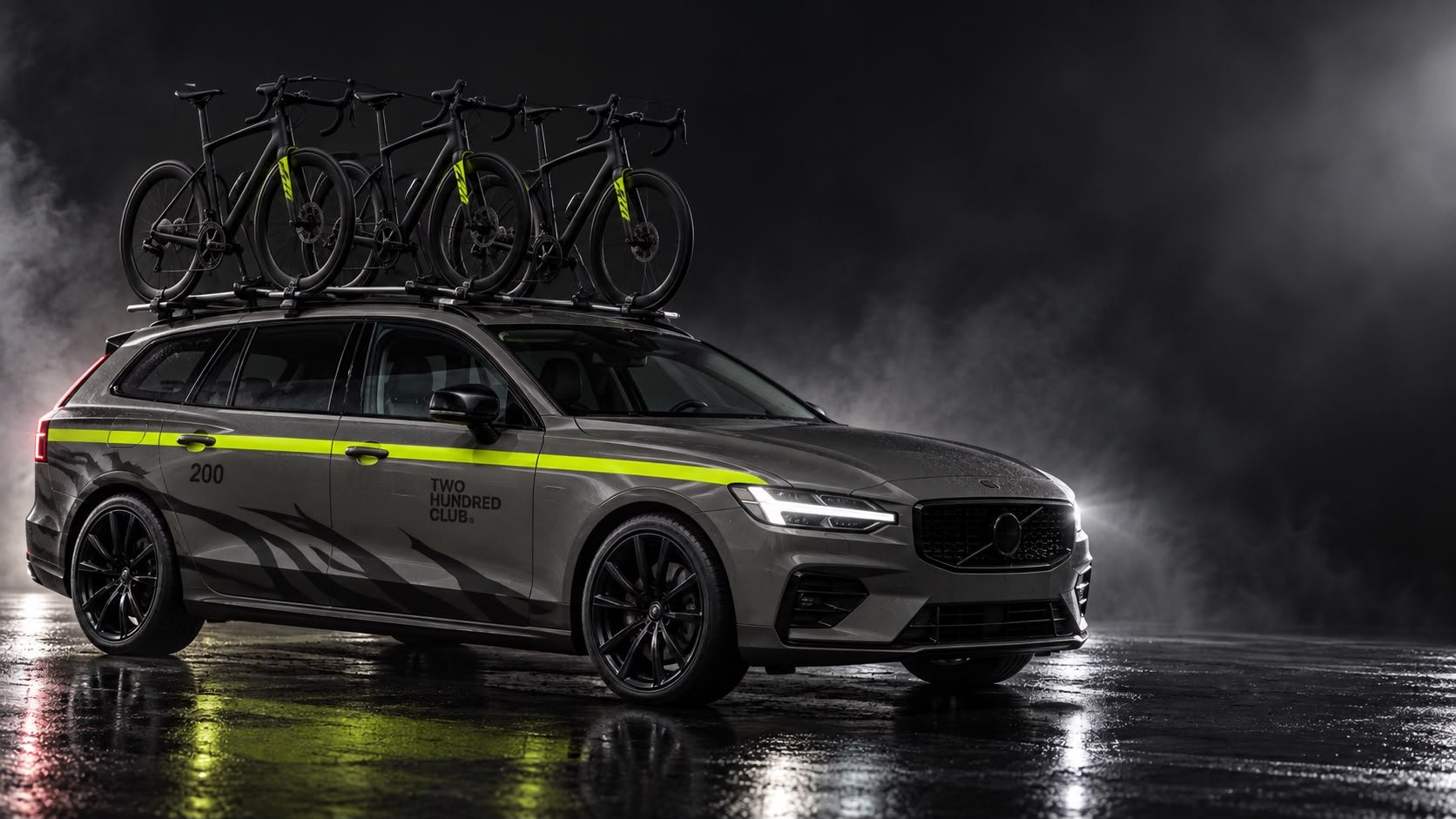 Carro de apoio cinzento com faixa lima, o número 200 na porta e três bicicletas no tejadilho.